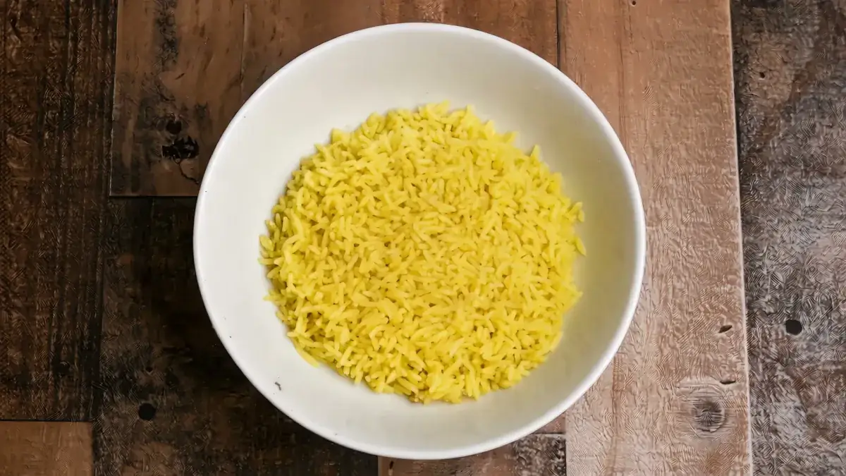 A white bowl of golden saffron rice on a wood table