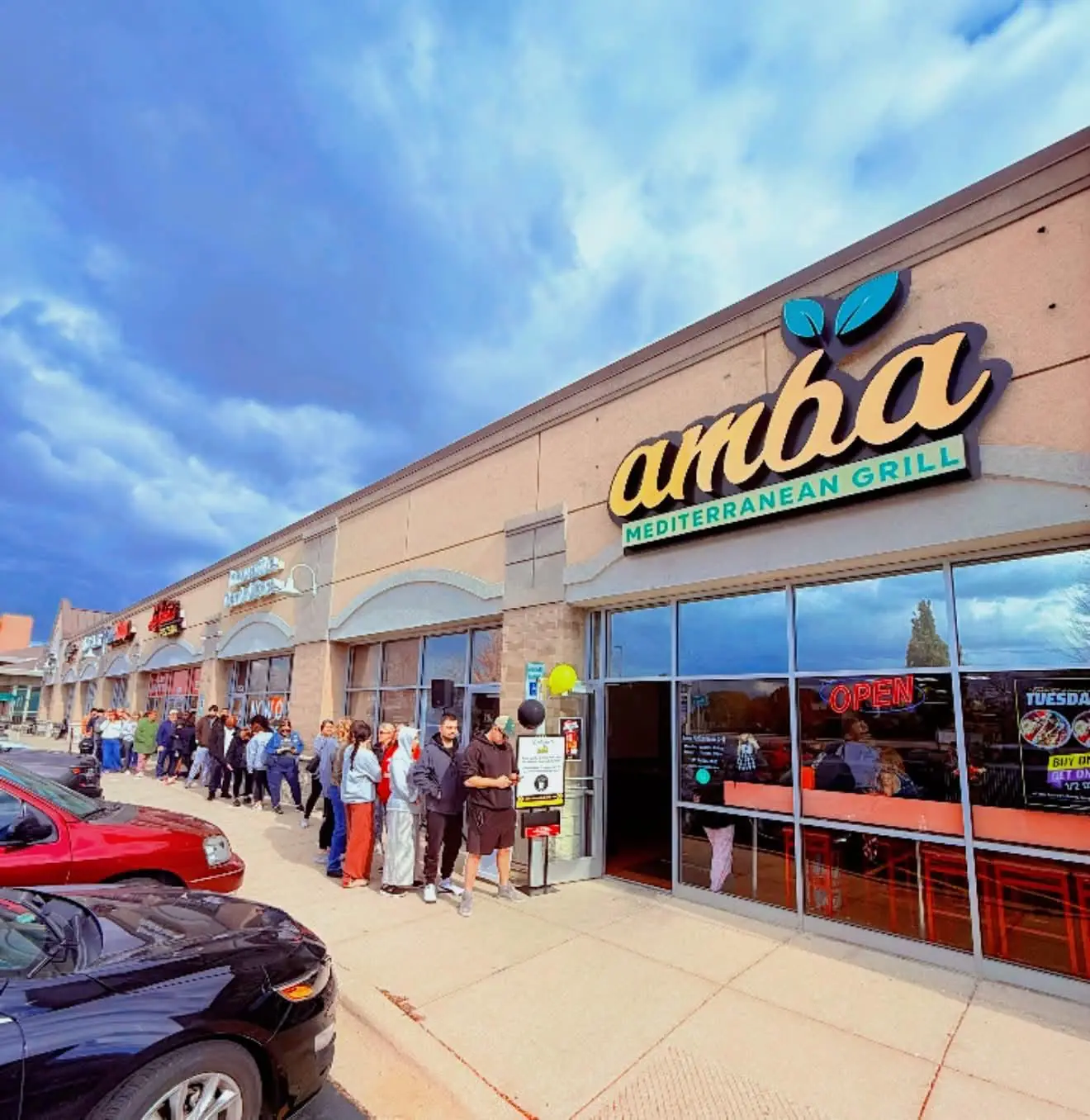 A line of guests outside the AMBA Mediterranean Grill storefront on a sunny day