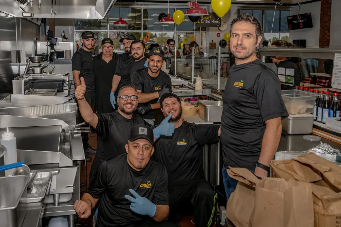 The AMBA crew in black AMBA shirts posing together in the kitchen